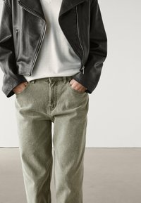 Svart läderkort jacka med dragkedja och fickor, i kombination med ljusgröna texturerade byxor med framfickor.