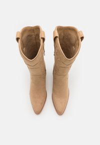 Botas de vaquero de ante de color canela con punteras puntiagudas, que presentan patrones de costura intrincados y dos lengüetas en la parte superior para facilitar su colocación.