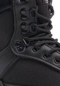 Black high-top boot featuring a canvas upper, plastic eyelets, and round laces. The design includes a padded collar and a smooth leather accent.