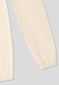 Jasno kremowe dresowe spodnie wykonane z miękkiego, elastycznego materiału. Posiadają elastyczne mankiety przy kostkach oraz gładkie wykończenie.