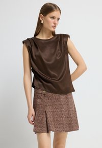 Brun satin top med draperet design, parret med en struktureret brun miniskørt med knapdetalje og et frontslids.