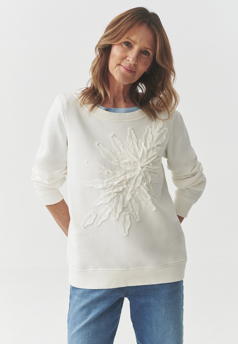 Felpa bianca con un design floreale testurizzato e sovrapposto sul frontale. Maniche e orlo a costine, abbinata a uno strato inferiore blu chiaro. Jeans in denim chiaro.