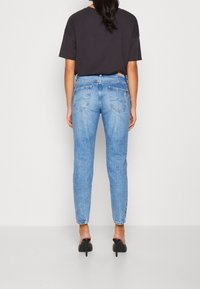 Jeans in denim blu con vestibilità slim, vita alta e lavaggio slavato. Presentano due tasche posteriori e una chiusura classica con bottone e zip. Abbinati a una maglietta nera.