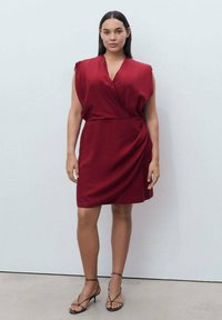 Short-sleeved, deep red dress with a wrap design, cinched waist, and soft fabric. Paired with strappy black sandals. Smooth texture.