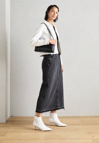 Maxifalda de mezclilla negra, chaqueta corta blanca, botas de cuero blancas hasta el tobillo con punta afilada y bolso estructurado negro.