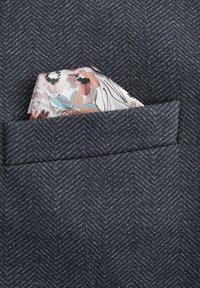 Crni herringbone materijal maramica za džep s cvjetnim uzorkom u svijetlim pastelno obojenim nijansama, koja viri iz džepa sakoa.