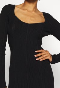 Schwarzes, geripptes Kleid mit carréförmigem Ausschnitt und langen Ärmeln, vertikalen Nahtdetails und taillierter Passform.