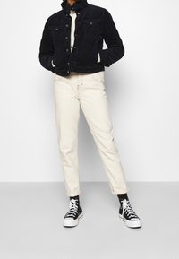 Navyblå corduroyjacka med två bröstfickor och metallknappar, tillsammans med beige rakbenbyxor och svarta högstövlade sneakers.