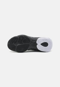 Semelle de chaussure avec bande de roulement en caoutchouc noir et blanc présentant des motifs et un logo central embossé sur un fond gris clair.