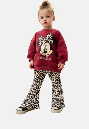 Mörkröd sweatshirt med en stor grafik av Minnie Mouse; beigefärgade leopardmönstrade utsvängda byxor; svarta sneakers med vita sulor.