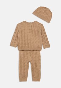 Beige kötött baba szett, amely tartalmaz egy kötött pulcsit fonott mintával, kerek nyakkal és gombos zárással, valamint hozzáillő fonott leggingset és sapkát.