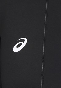 Tissu noir avec un logo ASICS blanc et un détail de couture verticale visible sur le côté droit.