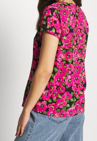 Koszulka z krótkim rękawem w kwiaty, z wyrazistymi różowymi kwiatami na czarnym tle, o prostym kroju i subtelnym szwem z tyłu.