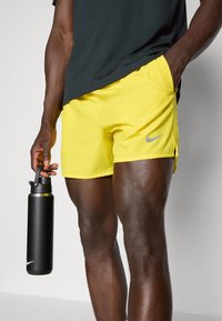 Yellow Nike athletic shorts with a sleek design, side slits, and a reflective silver logo, paired with a black water bottle.