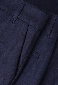 Tmavě modré kalhoty na míru vyrobené z denimu, s plisovaným předním dílem, plochým pasem a poutky na opasek, s hladkou texturou a jemným leskem.