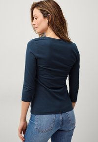Navyblaues Langarmshirt mit rundem Halsausschnitt, taillierter Passform und weicher Textur, kombiniert mit hellblauen Hochbundjeans.