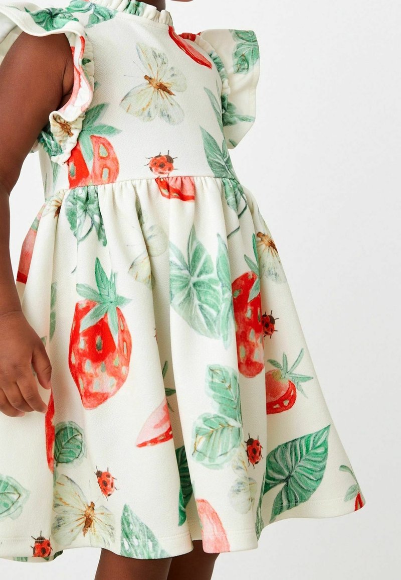 Robe blanche avec un motif floral et fruité en rouge, vert et jaune. Manches volantées et corsage ajusté avec une jupe évasée.