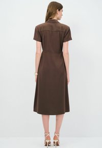 Robe marron à manches courtes avec col, jupe mi-longue et taille cintrée. La texture lisse et les lignes épurées mettent en valeur le design.