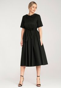 Czarna, krótko-sleeve sukienka z kołnierzykiem i zapięciem na guziki. Elastyczna talia z przewiązanym paskiem. Rozkloszowana, sięgająca kostek spódnica, wykonana z gładkiego materiału.