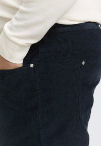 Navy Cord-Ripp-Hosen mit strukturierter Oberfläche, ausgestattet mit Seitentaschen und silbernen Akzenten. Der Bund ist elastisch für zusätzlichen Komfort.