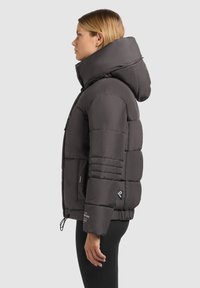 Svart puffjacka med hög krage, fickor med dragkedja och sidopaneldesigner. Tjock fyllning, slät yta och justerbar fåll.