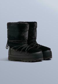 Sorte vinterstøvler med en blød, fnugget overdel, robust gummisål og snøresystem til justering. Tekstureret finish med en tyk manchet.