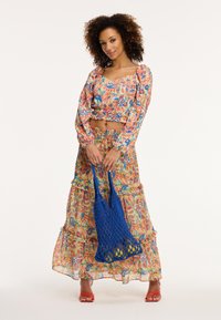 Virágmintás, két részes szett, amely egy cropped topból és egy réteges maxi szoknyából áll élénk színekben. Kék hálós táskával és narancssárga szandállal párosítva.