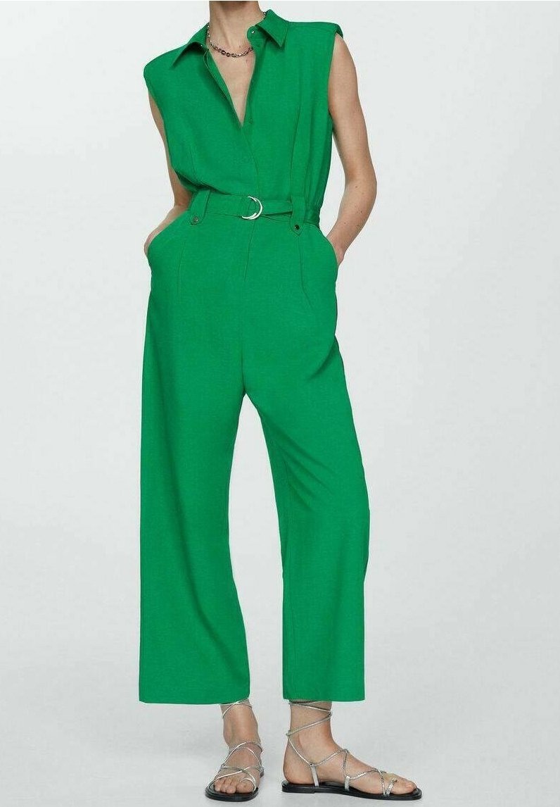 Combinaison verte sans manches avec col, taille ceinturée, coupe à jambes larges, texture lisse, complétée par des sandales argentées à lanières.