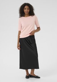 Haut tricoté rose pâle à manches courtes associé à une jupe maxi en satin noir et des ballerines noires, avec une texture lisse et un design simple.