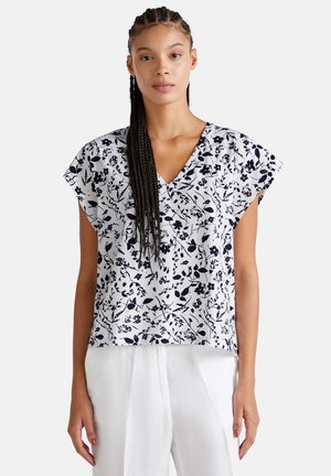 Blusa blanca de flores con estampado en azul marino, mangas cortas y diseño de escote en V, combinada con pantalones blancos de corte holgado y tejido suave.
