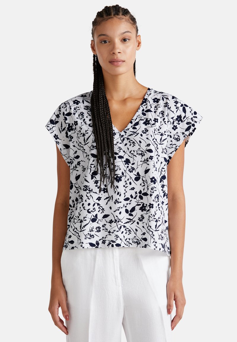 Blusa blanca de flores con estampado en azul marino, mangas cortas y diseño de escote en V, combinada con pantalones blancos de corte holgado y tejido suave.