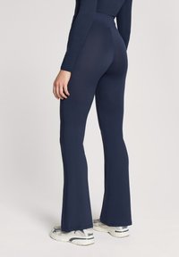 Granatowe legginsy dzwonowate wykonane z elastycznego materiału, z wysokim pasem i gładką fakturą, w połączeniu z białymi butami sportowymi.