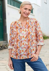 Luftige, gemusterte Bluse mit orangen, pinken und hellblauen Blumenmotiven, Knopfleiste und Dreiviertelärmeln, kombiniert mit Jeans.