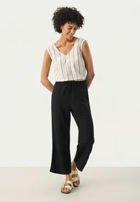 Lightweight striped sleeveless top in beige and dark brown; black loose-fitting trousers with an elastic waistband; beige sandals.