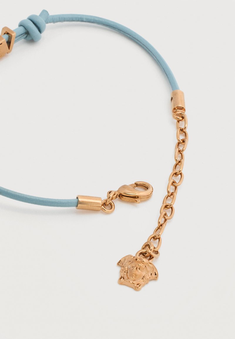 Light blue cord bracelet with a gold-tone chain extender and a small Medusa head charm near the lobster clasp closure.