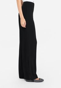Pantalones negros de cintura alta con corte recto y abertura lateral, hechos de una tela suave. Llevados con zapatos planos negros con acentos de brillantina.