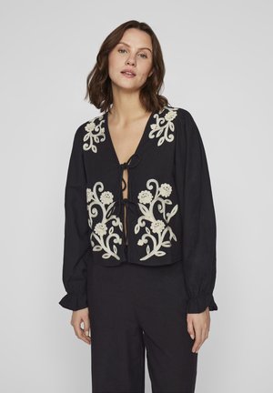 Black cropped blouse with long sleeves and a V-neck. Features white floral embroidery and a tie-front detail. Soft fabric with gathering at sleeves.