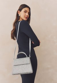 Bolso plateado con superficie texturizada cubierta de cristales multicolores, con asa superior y correa ajustable para el hombro.