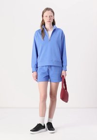 Lichtblauwe sweatshirt met een ritskraag, gecombineerd met bijpassende shorts. Zwarte sneakers en een rode handtas maken de look compleet.