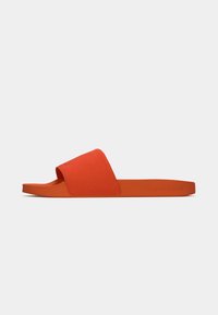 Une sandale slide orange avec une large bride en tissu et une semelle plate, vue de côté sur fond uni clair.