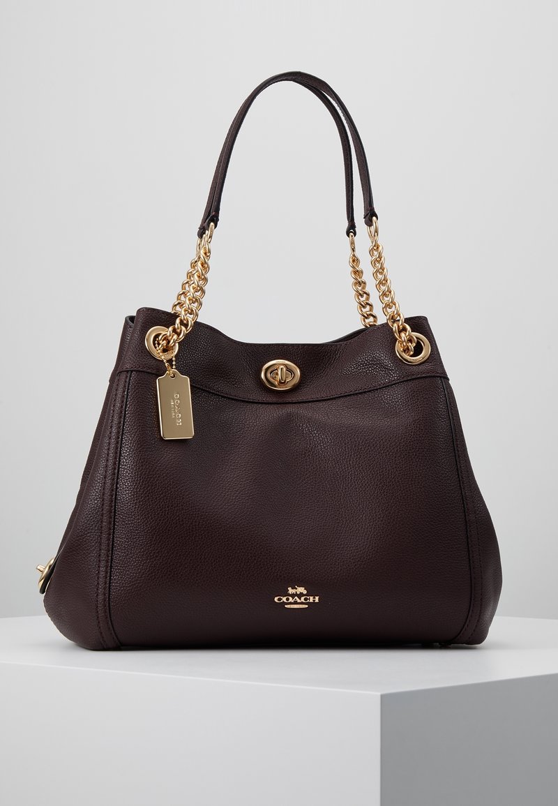 Ciemnobrązowa skórzana torebka o fakturowanym wykończeniu, z paskami łańcuchowymi w kolorze złota, wyrazistym zapięciem i oznakowaną metką. Pojemny, zaokrąglony fason.