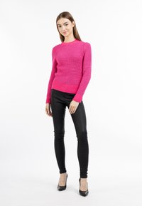 Pullover rosa neon lavorato a maglia con un motivo texturizzato, polsini e orlo a coste, abbinato a pantaloni neri aderenti e tacchi alti neri.
