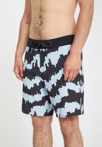 Bañadores en azul claro con un patrón abstracto negro. Presentan una cintura negra con cordón y bolsillos laterales. Hechos de material de secado rápido.