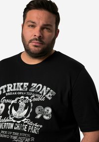 Černé bavlněné tričko s grafickým potiskem a bílým textem, včetně "STRIKE ZONE" a detailů s baseballovou tematikou. Klasický design s kulatým výstřihem.