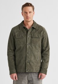 Olivgrüne Cordjacke mit Kragen, zwei Brusttaschen und Knopfverschluss. Weicher Stoff; funktionales Design, das sich gut zum Schichten eignet.