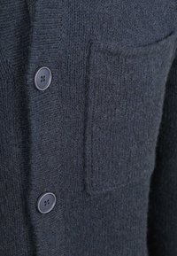 Donkerblauwe cardigan van textuurgebreid materiaal, met een patchzak en een sluiting met vier knopen van ronde, donkere kunststof knopen.