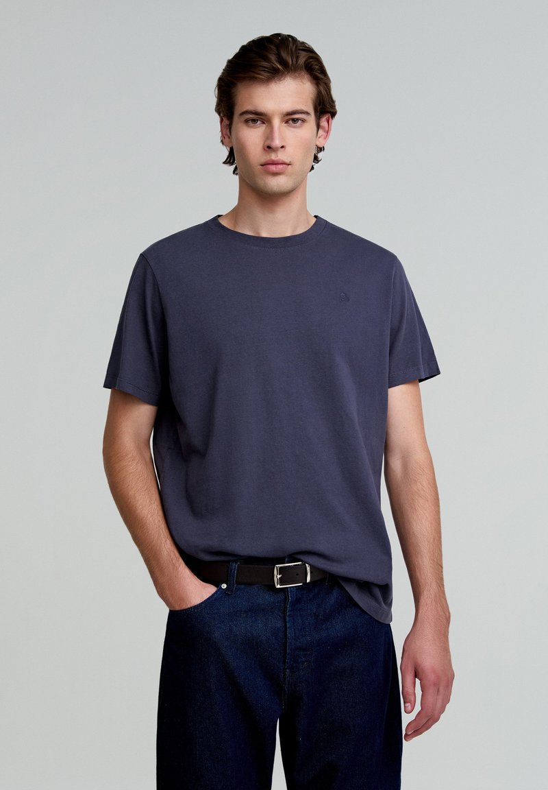 Tricou din bumbac de culoare bleu marin, cu gât rotund, mâneci scurte și un logo mic pe piept. Purtați-l cu blugi denim închis și o curea neagră.