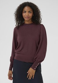 Burgundy knit sweater with puffed long sleeves and button accents at the cuffs. Features a round neckline and a relaxed fit.
