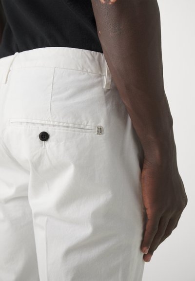 Pantaloni bianchi in cotone con taglio classico, dotati di una tasca posteriore con bottone e un piccolo dettaglio metallico. Il tessuto presenta una leggera texture.