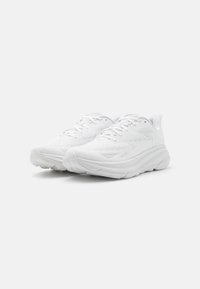 Zapatillas deportivas blancas con una parte superior de malla transpirable, suela gruesa y acolchada, detalles texturizados y puntera reforzada.